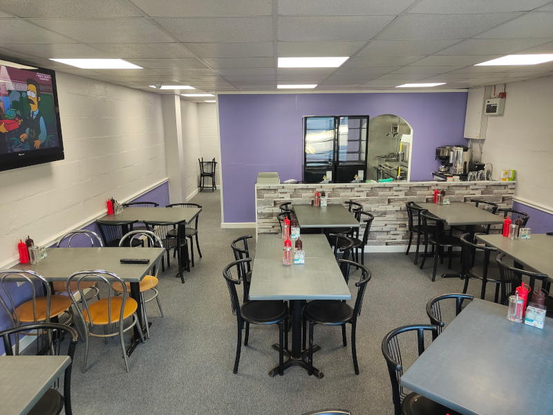 The Greasy Fork cafe interior with grey tables, black chairs, purple accent wall, and display refrigerator